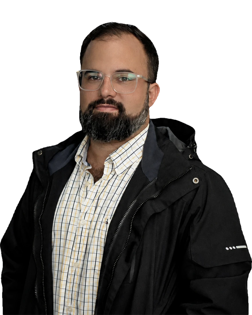 Bernardo Toro, in glasses and a dark jacket over a checked shirt, against a dark ground.